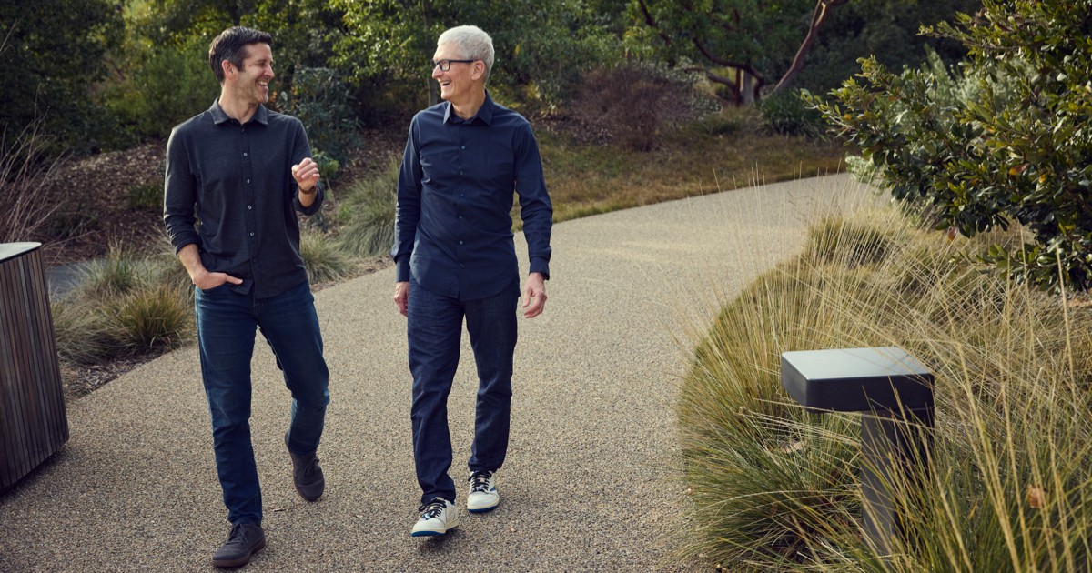 Tim Cook, cheveux argentés et lunettes, marche dans la végétation d'Apple Park aux côtés de John Ternus, son successeur, tous deux souriants.